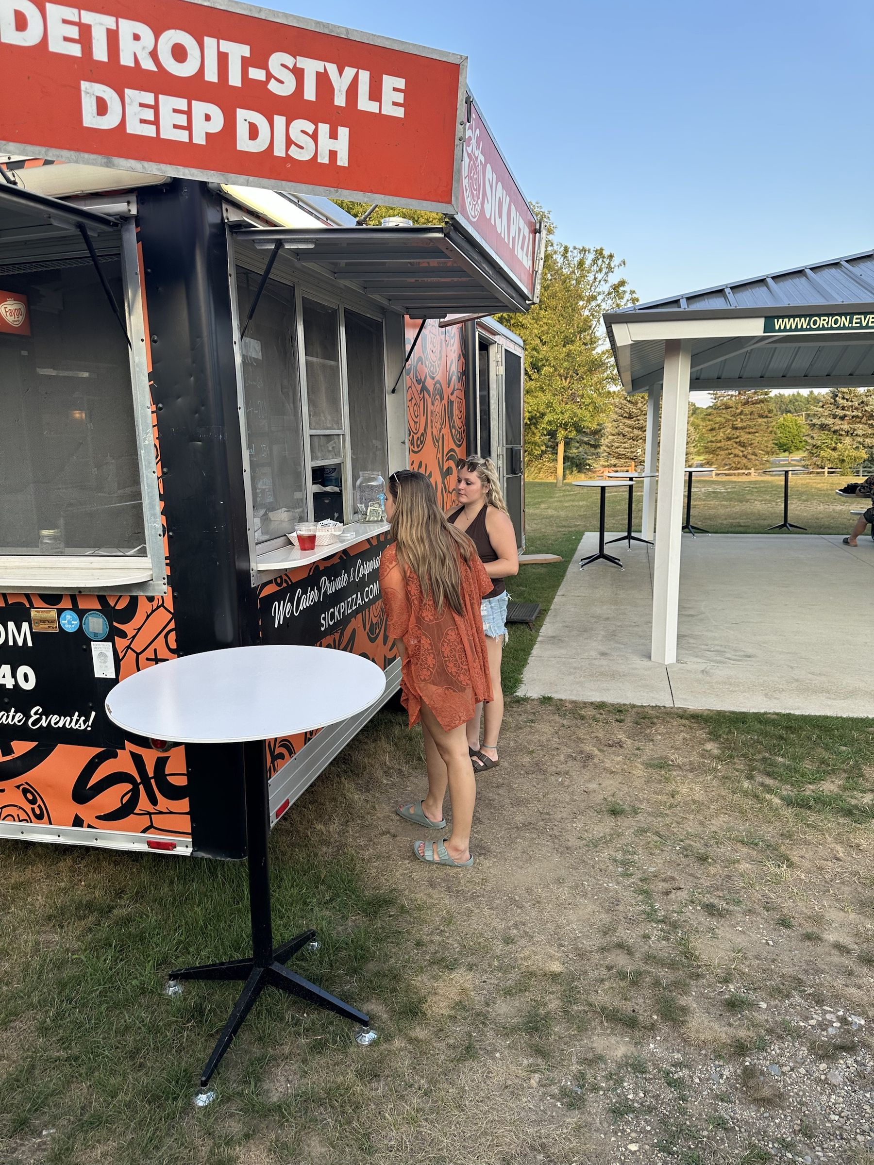 Two guests ordering at the Sick Pizza trailer window